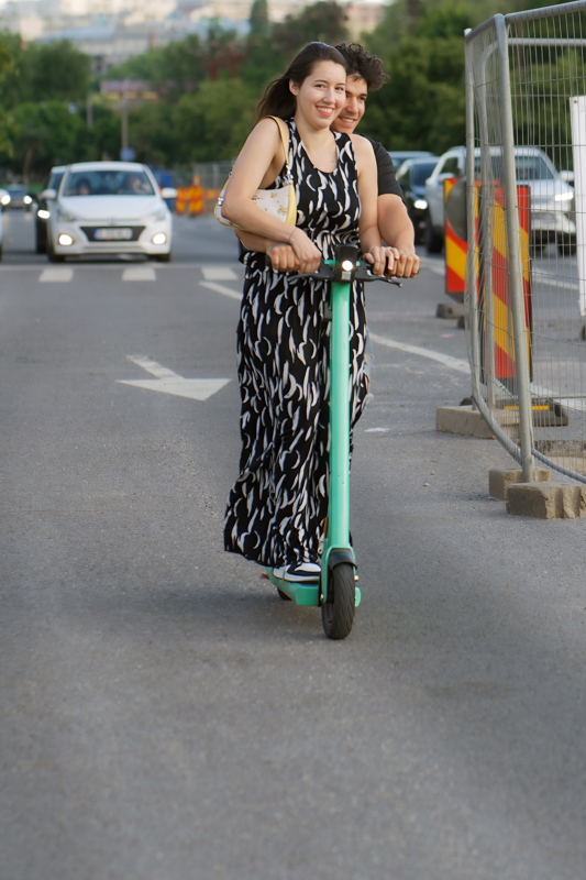 5 - Two people riding a bright green Bolt electric scooter down a paved road